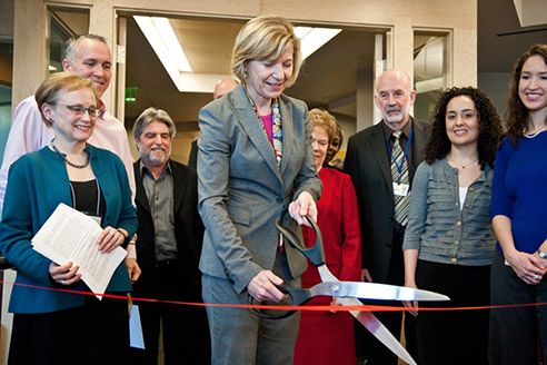 Desmond-Hellmann cuts a red ribbon with giant scissors while others watch