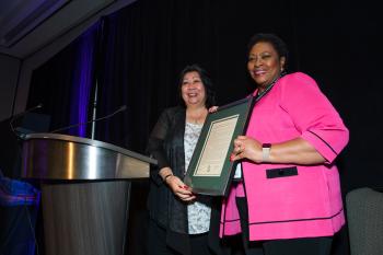 Wong presents framed award to Kennedy on stage.