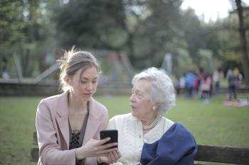 on a park bench a young woman shows an older woman a cellphone.