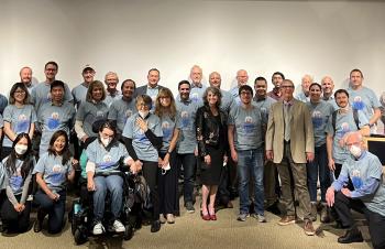 Wells and Arkin standing with a more than a dozen people in blue shirts